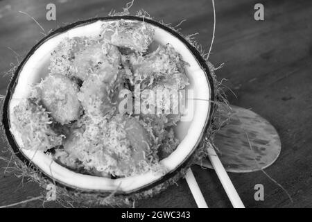 Eine Graustufenaufnahme von würfelgeschnittenen Bananen, die in eine alte Kokosnuss eingelegt wurden Stockfoto