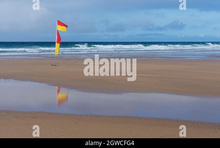 RNLI-Flaggen an einem Strand kennzeichnen den sicheren Bereich zum Schwimmen oder Surfen. Reflexionen sind im Vordergrundwasser zu sehen Stockfoto