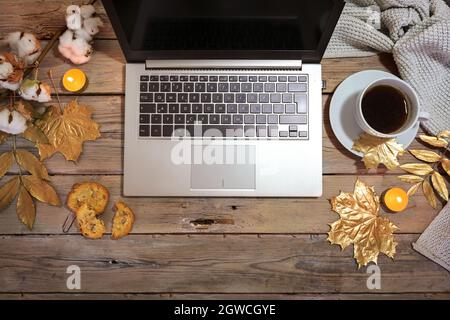 Laptop-Computer und Kaffeetasse auf einem rustikalen Holztisch mit goldlackierten Herbstblättern und Kerzen verziert, gemütliches Heimbüro, flach von oben, Stockfoto