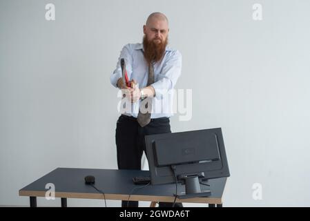 Gestresste verrückte Geschäftsmann zerschlagen seinen Computer im Büro mit Axt Problem Konzept. Der Mann hat Probleme bei der Arbeit und Frustration. Stockfoto