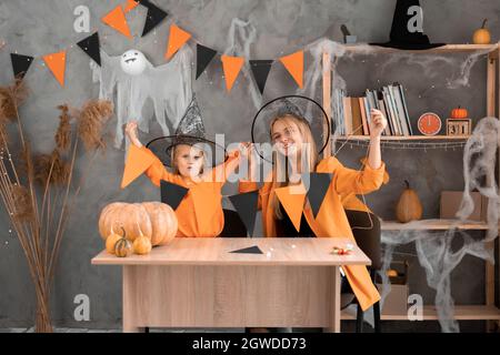 Mutter und Tochter machten zu Hause mit ihren eigenen Händen eine Girlande aus orangefarbenen und schwarzen Fahnen für Halloween. Stockfoto