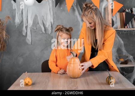 Eine Frau und ein Mädchen in machen aus großen Kürbissen eine Jack-o-Laterne für die Feier von halloween. Mit einem Messer schneiden und das Fruchtfleisch mit den Samen herausnehmen. Stockfoto