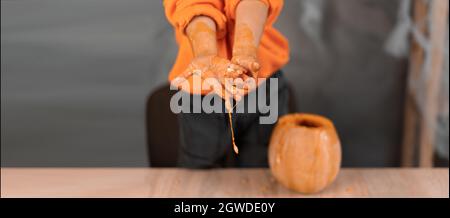 Halloween macht Jack O'Lantern zu Hause. Kürbiszubereitung. Kinderhände bekommen Samen aus dem Kürbis. Halloween-Konzept. Stockfoto