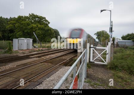 Unbemannte Bahnüberfahrt am Bahnhof Buckenham mit einem Zug der British Rail-Klasse 755, der mit hoher Geschwindigkeit in Richtung Bahnhof Norwich fährt. Stockfoto