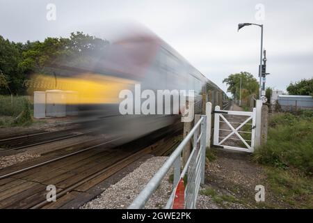 Unbemannte Bahnüberfahrt am Bahnhof Buckenham mit einem Zug der British Rail Klasse 755, der mit hoher Geschwindigkeit in Richtung Norwich Station fährt. Stockfoto