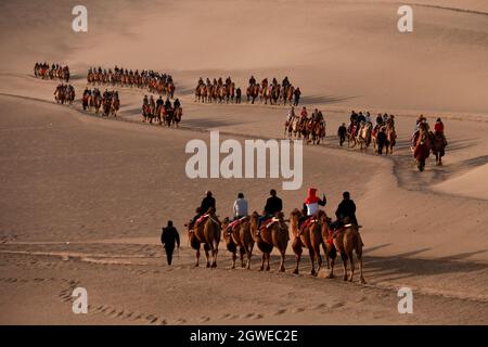 Dunhuang, Chinas Provinz Gansu. Oktober 2021. Touristen reiten auf Kamelen im malerischen Gebiet des Mingsha-Berges und der Halbmond-Quelle während des laufenden Nationalfeiertags in Dunhuang, nordwestlich der chinesischen Provinz Gansu, am 3. Oktober 2021. Quelle: Zhang Xiaoliang/Xinhua/Alamy Live News Stockfoto