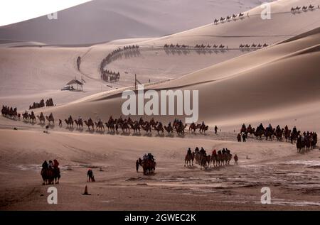 Dunhuang, Chinas Provinz Gansu. Oktober 2021. Touristen reiten auf Kamelen im malerischen Gebiet des Mingsha-Berges und der Halbmond-Quelle während des laufenden Nationalfeiertags in Dunhuang, nordwestlich der chinesischen Provinz Gansu, am 3. Oktober 2021. Quelle: Zhang Xiaoliang/Xinhua/Alamy Live News Stockfoto