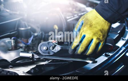 Kfz-Mechaniker, der Steckschlüssel und Werkzeuge an der Karosserie in der Reparaturwerkstatt aufnimmt Stockfoto