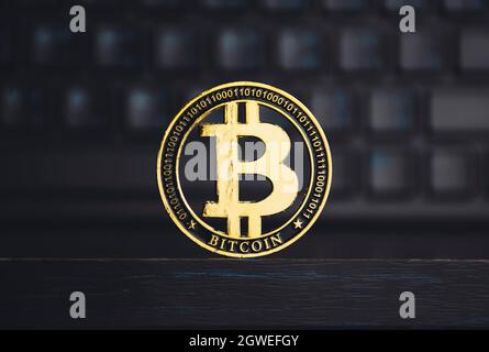 Nahaufnahme der goldenen Bitmünze auf dem Holztisch mit einem verschwommenen Tastaturhintergrund, Krypto-Währungskonzept. Stockfoto