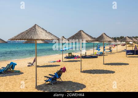 Der wunderschöne weiße Sandstrand von Griechenland mit leeren Sonnenliegen und Sonnenschirmen ist wunderschön. Türkisfarbenes Meerwasser und blauer Himmel. Schöner Hintergrund. Griechenland. Stockfoto