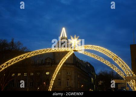 Der traditionelle Weihnachtsbogen an der Düsseldorfer Königsallee mit dem historischen beleuchteten Deutsche Bank-Gebäude im Hintergrund. Stockfoto