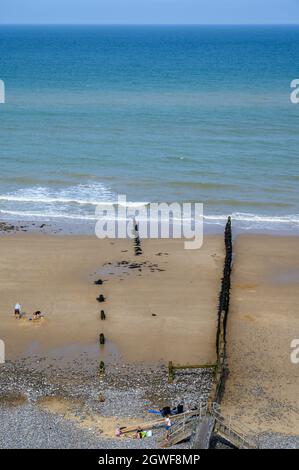 Ein paar Leute genießen sich neben Groynes an einem ansonsten leeren Abschnitt des Cromer Beach, Norfolk, England. Stockfoto