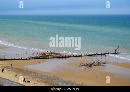 Ein paar Leute genießen sich neben einem Groyne auf einem ansonsten leeren Stück Cromer Beach, Norfolk, England. Stockfoto