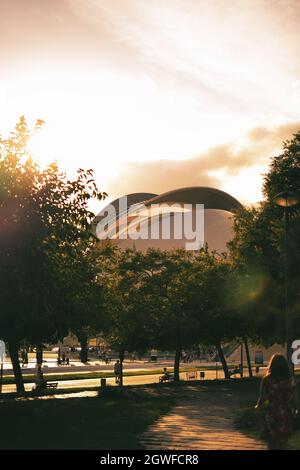 Eine vertikale Aufnahme eines Parks in der Nähe des runden Gebäudes, Menschen gehen und sitzen Stockfoto
