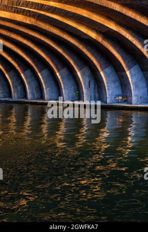 Sonnenbeschienenen geschwungenen Linien unter der alten Eisenbahnbrücke bei Sonnenuntergang, abstrakter Bogen Ziegel und Stein Struktur mit Reflexion im Wasser, Berlin, Deutschland. Stockfoto