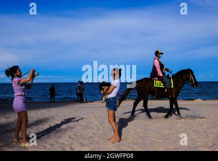 Eine junge Frau mit einem kleinen Hund posiert für ein Foto am Hua hin Strand in Thailand Stockfoto