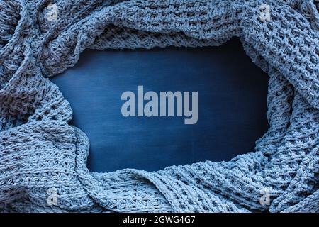 Grau gewebte Decke zerknittert und gerahmt auf einem blau getönten schwarzen Holzhintergrund. Aufnahme von oben mit freiem Platz für Hintergrundtext. Stockfoto