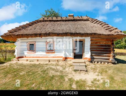 Traditionelles ukrainisches Landhaus mit Strohdach und Weidenzaun an einem warmen Sommertag vor einem blauen Himmel mit weißen Wolken. Speicherplatz kopieren. Stockfoto