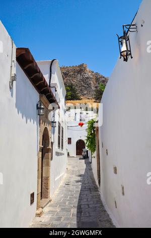 Weiße schmale Straße von Lindos. Griechisches Dorf während des sonnigen Sommertages auf Rhodos. Stadtansicht der Akropolis in Griechenland. Stockfoto