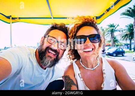 Porträt eines fröhlichen kaukasischen Paares, das während einer Autoreise Urlaub genießt. Glückliches Paar, das während ihrer Reise lacht. Fröhliches Paar, das Selfie auf V Stockfoto