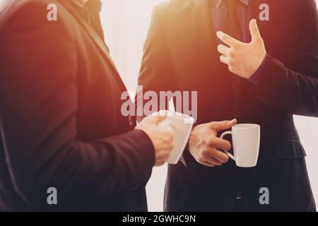 Zwei Geschäftsleute stehen im Gespräch zusammen mit einem Kaffeebecher am Morgen in der Hand. Stockfoto