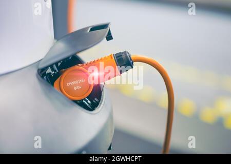 EV Auto oder Elektroauto an der Ladestation mit eingesteckter Stromkabelversorgung, modernes umweltfreundliches, energiefahrendes Fahrzeug Stockfoto