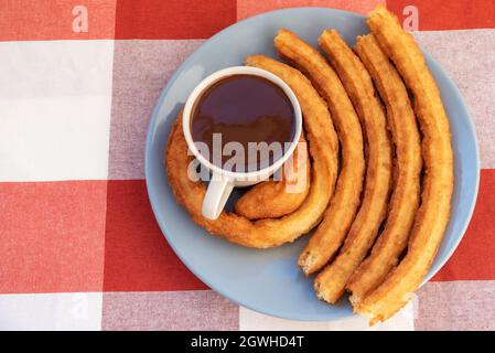 Teller mit einer Tasse Schokolade und Churros rund um die Tasse, Frühstück oder Snack in Andalusien, Spanien. Stockfoto