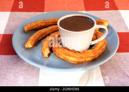 Teller mit einer Tasse Schokolade und Churros rund um die Tasse, Frühstück oder Snack in Andalusien, Spanien. Stockfoto