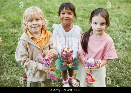 Hochwinkelporträt von drei niedlichen Kindern, die Süßigkeiten von Pinata halten und während der Geburtstagsfeier im Freien lächeln Stockfoto