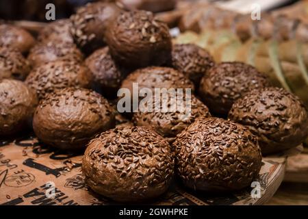 Schwarze runde Brötchen, mit Getreide bestreut. Frisches Gebäck, braune kleine Burger in der Bäckerei. Stockfoto