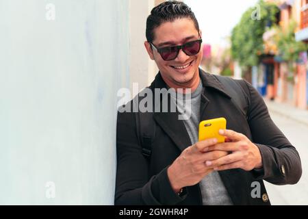 Hispanischer Mann, der mit dem Handy die Straße entlang läuft Stockfoto