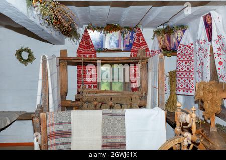 Design und Interieur der Räumlichkeiten einer alten ländlichen Hütte mit Webstuhl und Spinnrad im traditionellen ukrainischen Stil. Stockfoto
