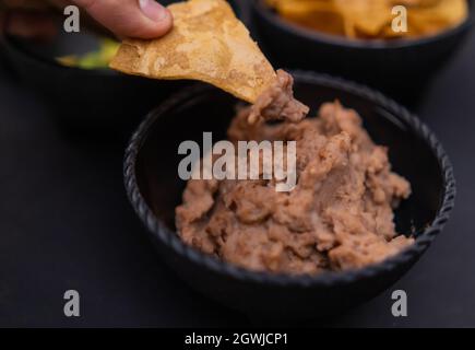 Von Hand eintauchen Tortilla Chip in eine Schüssel mit gebratenen Bohnen Stockfoto