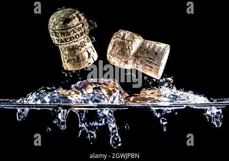 Zwei Korkstopfen fliegen durch die Wasseroberfläche und spritzen Wasser auf schwarzem Hintergrund. Prosecco-Weinstöpsel aus der Region Valdobbiadene, Italien. Stockfoto