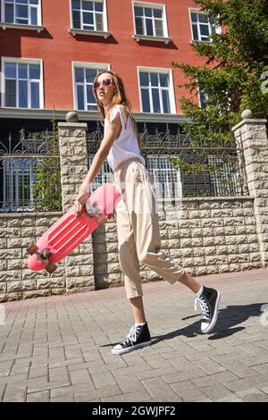 Mädchen mit Skateboard. Stadtlandschaft. Schwarze Sneaker. Neuer Normalweg Stockfoto