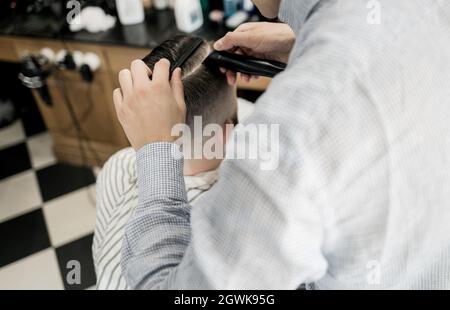 Ein Friseur schneidet sich die Haare, indem er eine Nahaufnahme des Haarschnitts eines Mannes erstellt. Friseurhands und arbeiten an den Haaren des Kunden. Hintergrund. Friseurgeschäft Konzept. Herren Stockfoto