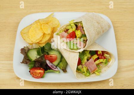 Speck, Salat und Tomatenpackungen mit Salat und Kartoffelchips auf einem Teller auf einer Holzplatte Stockfoto