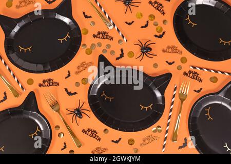 Schwarze katzenförmige Halloween Party Pappteller, Fledermäuse und Happy Halloween Text Konfetti auf orangefarbenem Hintergrund Stockfoto