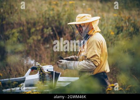 Imker in Schutzkleidung arbeiten in seinem Bienenhaus. Bienenzuchtkonzept Stockfoto