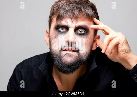 Porträt eines bärtigen Mannes mit untotem Make-up, der seine Hand in der Nähe seines Kopfes hält Stockfoto