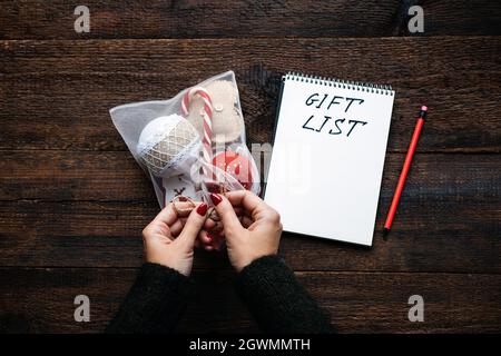 Weihnachtsgeschenk Liste, verfolgen Geschenke weihnachtszeit. Weibliche Hände mit offenem Notizblock und Text-Geschenkliste auf Holzhintergrund Stockfoto