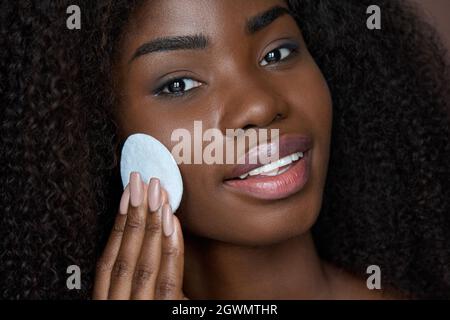 Schwarze junge Frau hält Wattepad entfernen Gesicht Make-up mit Make-up-Entferner. Stockfoto