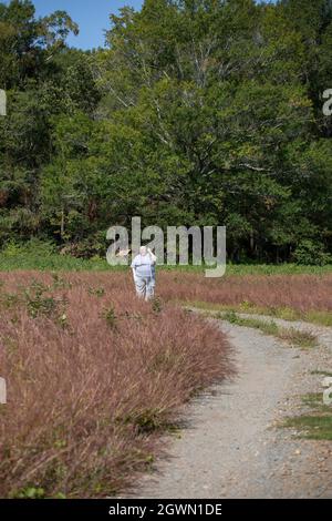 Albino-Frau, die auf einem kurvenreichen Kiesweg durch eine Wiese läuft Stockfoto