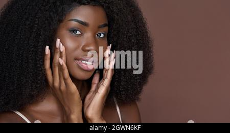 Junge schwarze Schönheit Mädchen berühren Gesicht isoliert auf braun. Kopfbild im Porträt. Stockfoto