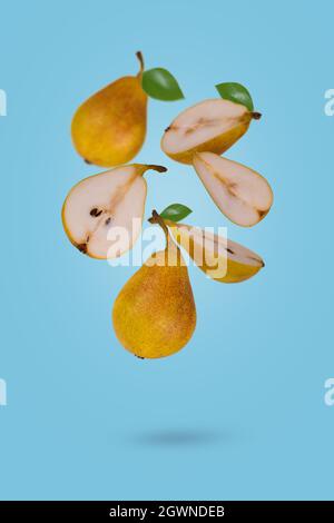 Frisch reife ganze und geschnittene Birnen fliegen in Luft isoliert auf blauem Hintergrund. Kreatives und minimalistisches Lebensmittelkonzept. Stockfoto