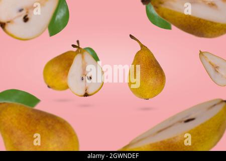 Frische reife ganze und in Scheiben geschnittene Birnen fliegen in der Luft isoliert auf einem rosa Hintergrund. Kreatives und minimalistisches Lebensmittelkonzept. Stockfoto