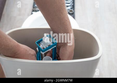 Installation von Wasserleitungen. Der Klempner installiert eine Spülpumpe in der Toilettenzisterne. Stockfoto