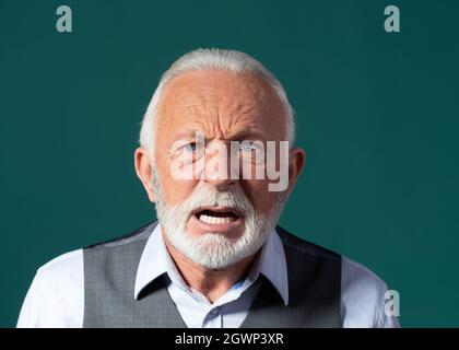 Porträt eines älteren Mannes in einem Geschäftsanzug, der schrie, sich wütend fühlte, frustriert war. Unzufriedener älterer Bürger mit blauen Augen und weißen Haaren und Bart dagegen Stockfoto