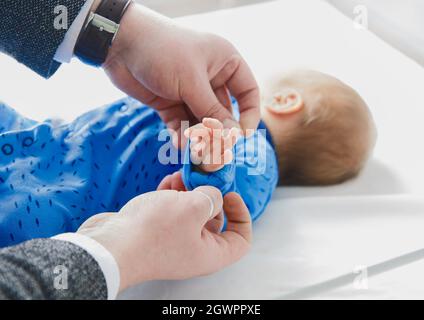 Die Hände des Vaters Rollen die Ärmel auf die Hand des Babys, Nahaufnahme. Neugeborenes Kind im Krankenhaus, Liebe und Pflege des Vaters der Eltern. Stockfoto