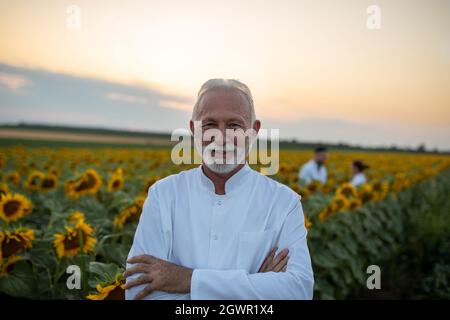 Zwei Agronomen stehen im Sonnenblumenfeld und reden im Hintergrund. Leitender Biologe, der lächelt und mit gekreuzten Armen auf die Kamera blickt. Stockfoto